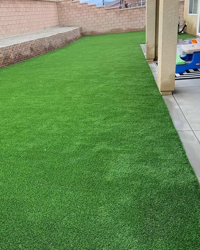 Bright green artificial turf side lawn beside a covered patio with a kids' play table