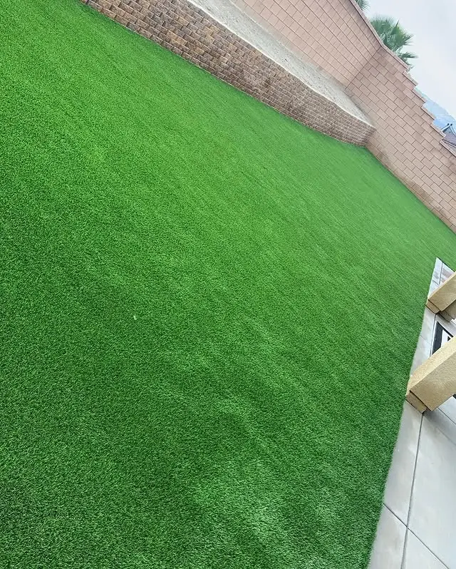 Spacious artificial turf backyard lawn framed by a brick retaining wall